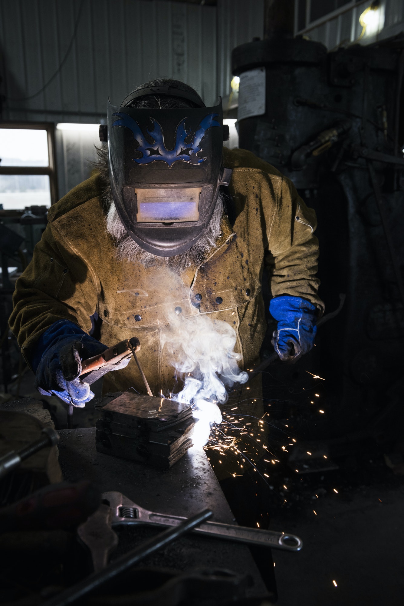 blacksmith in welding mask welding metal in workshop